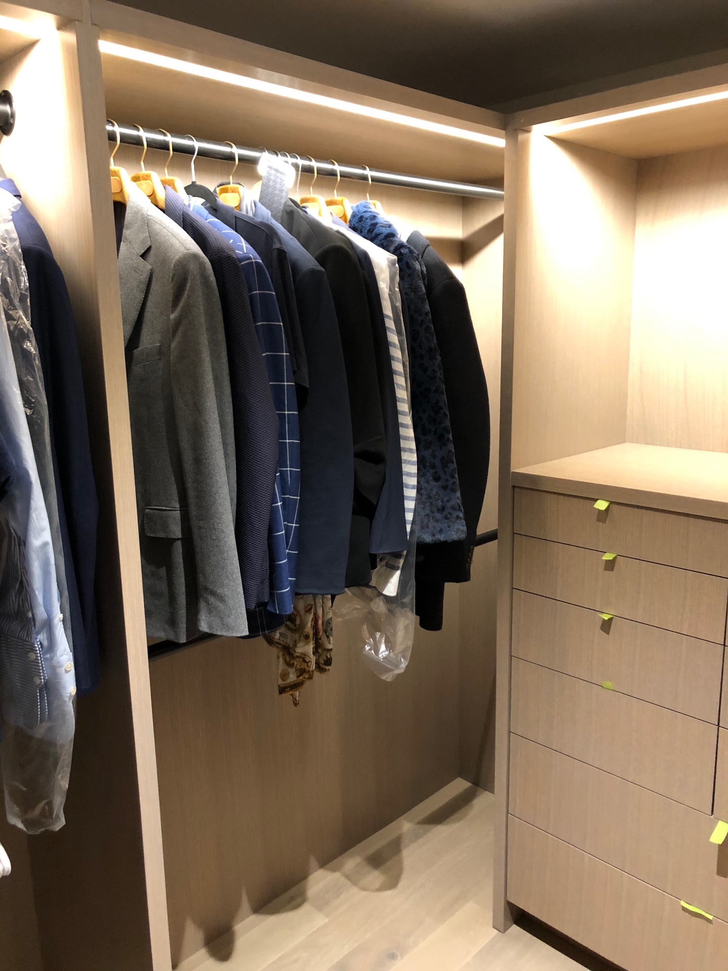 Parede de varões com casacos e camisas, bloco de gavetas à direita