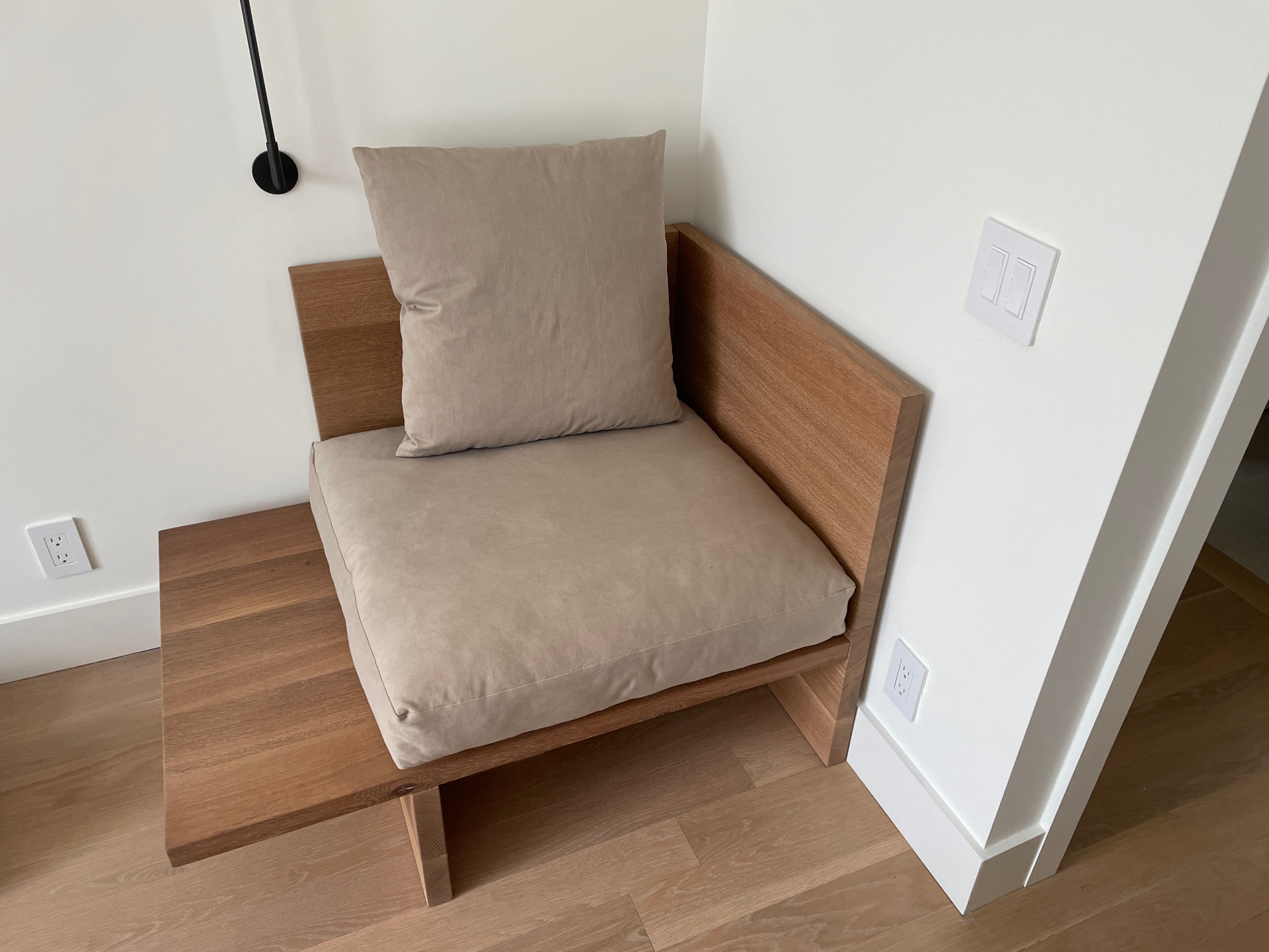 Oak chaise with single back cushion under a black wall sconce