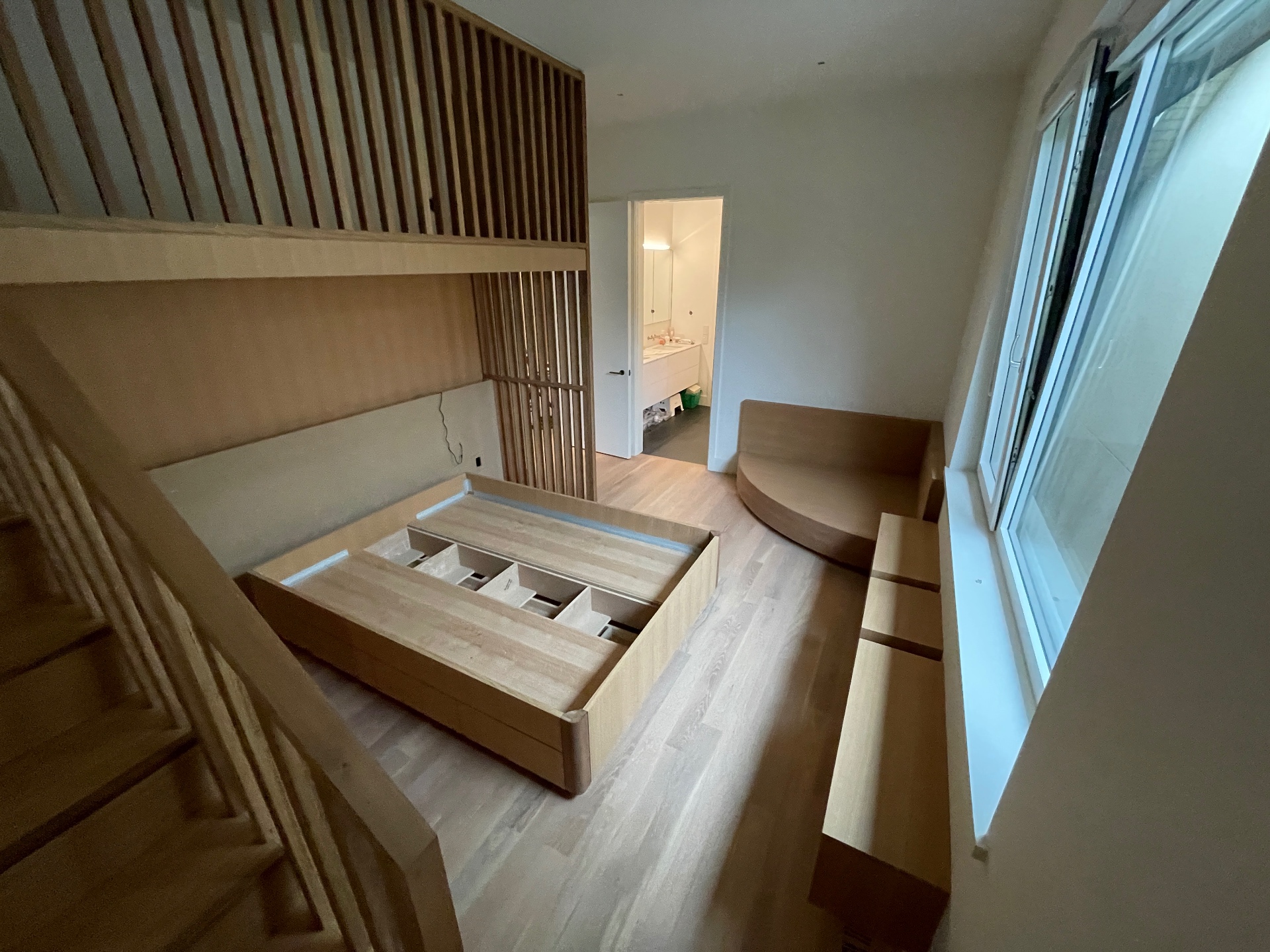 Oak loft bed volume with slatted guardrail and bathroom beyond