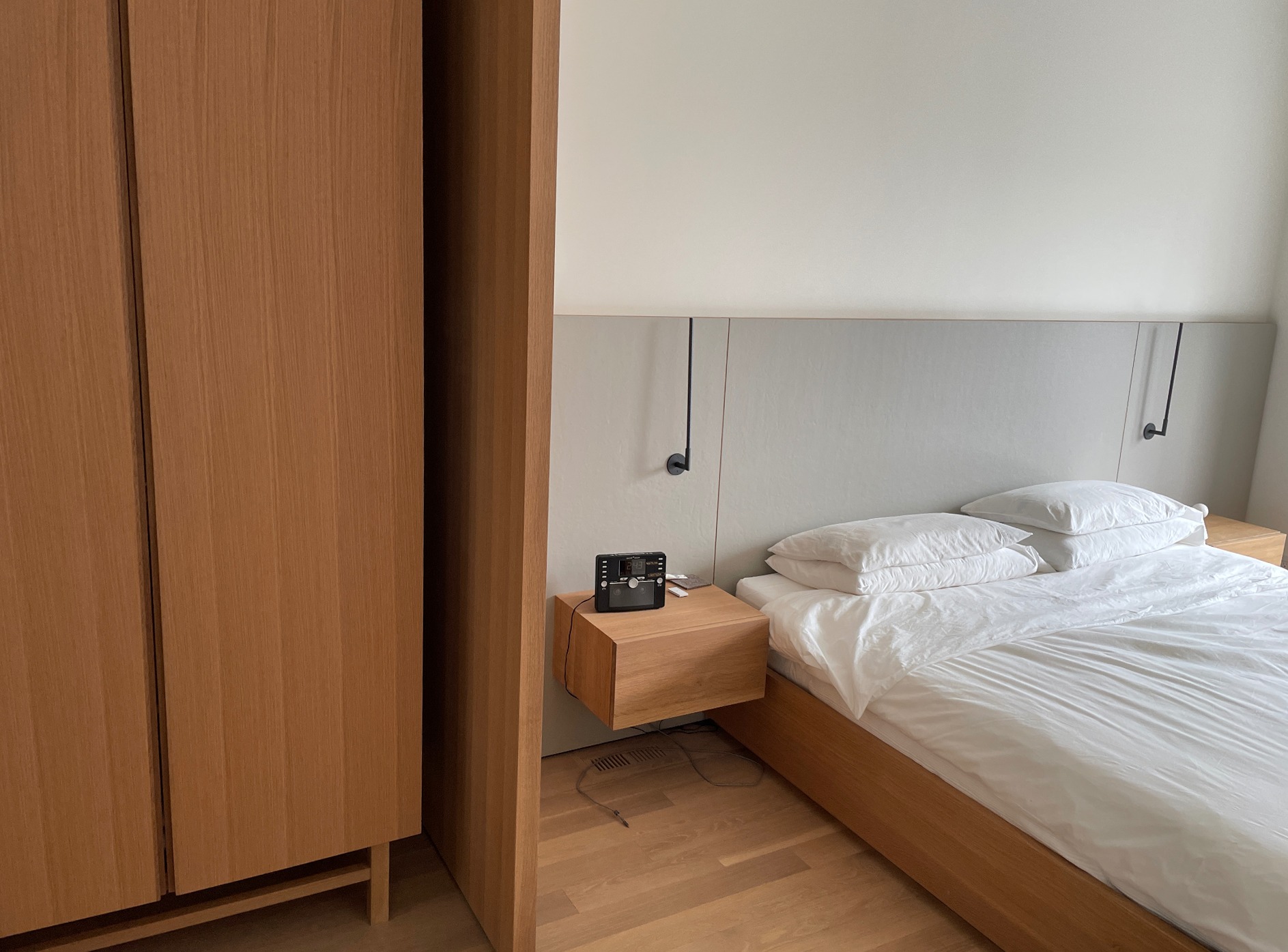 Canto do quarto com o armário de roupa em carvalho ao lado da cama e da mesa suspensa